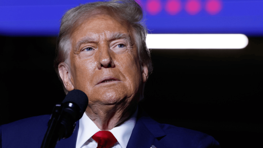 Close-up of President Trump, the elected 47th President of the USA in a suit and red tie speaking into a microphone, set against a background featuring blue and purple tones with blurred lights.