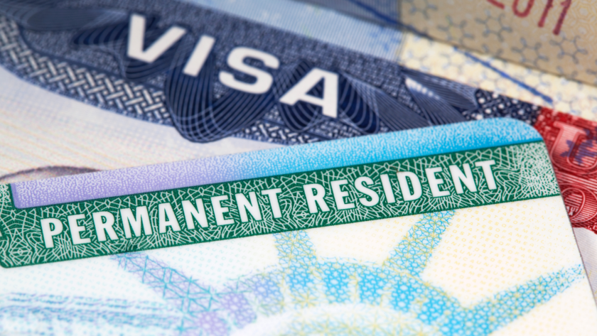 A close-up of a U.S. Permanent Resident Card (Green Card) placed on top of a visa document.