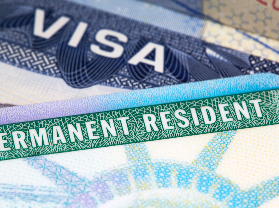 A close-up of a U.S. Permanent Resident Card (Green Card) placed on top of a visa document.